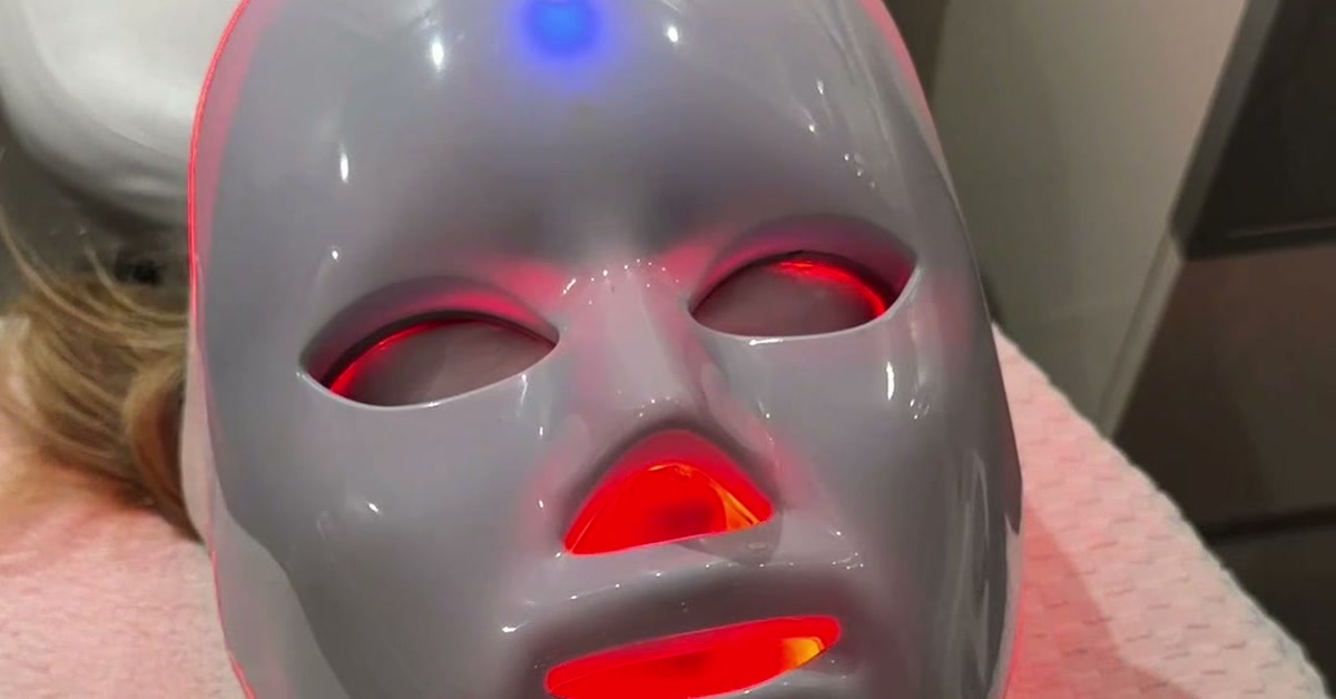 A client lies on a treatment bed at ROW 89 wearing a gray LED light-therapy mask that glows red at the eyes, nose and mouth