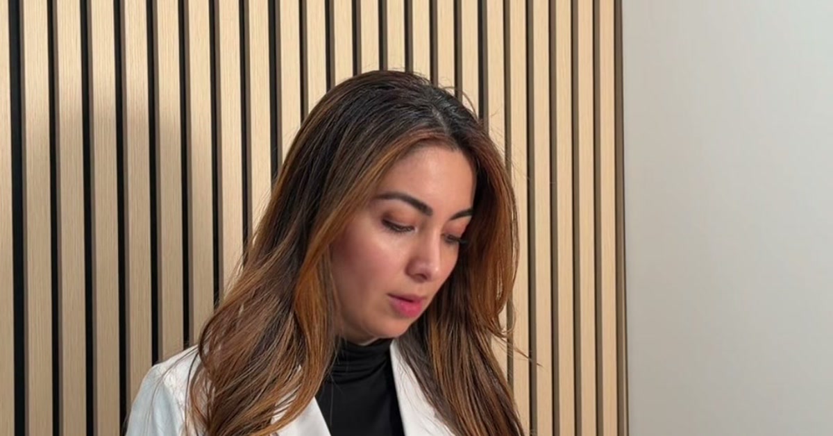 Rocio Romero, PA-C, in a white coat and black turtleneck, looking down in front of ROW 89's wood-slat wall