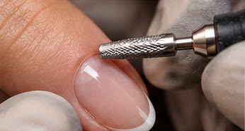 Close-up of an electric nail file bit working near the cuticle of a sheer pink nail